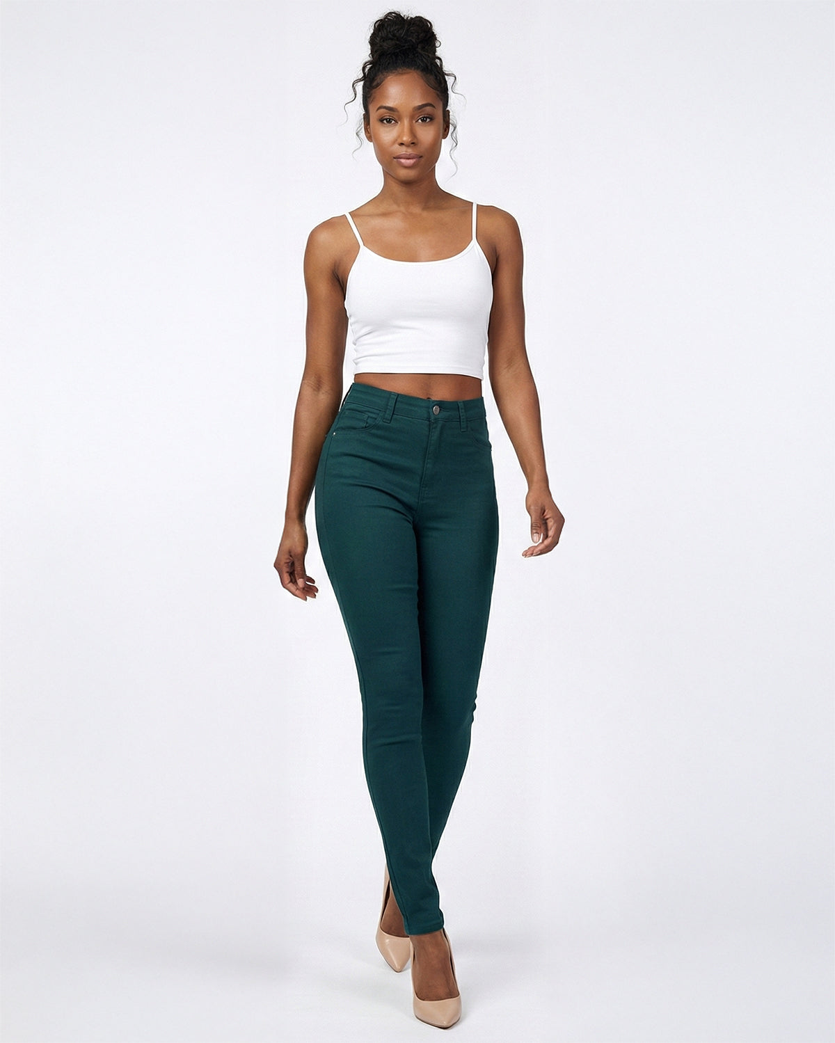 Woman wearing a white tank top and deep forest green skinny jeans 